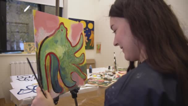 Woman painter with easel holding art brush in bright light art studio — Stock Video