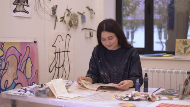 女艺术家笑着与阅读书籍明亮的灯光艺术工作室 — 图库视频影像