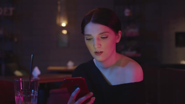 Vrouw met telefoon in de hand op de achtergrond van de bar interieur in neon lichten — Stockvideo