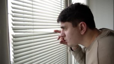 Evdeki adam panjurlardan dışarı bakıyor.