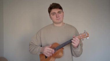 Bej arkaplanda ukulele olan müzisyen.