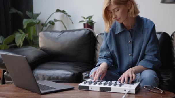Kobieta siedzi na czarnej kanapie nagrywania muzyki z laptopem, gra na klawiaturze — Wideo stockowe