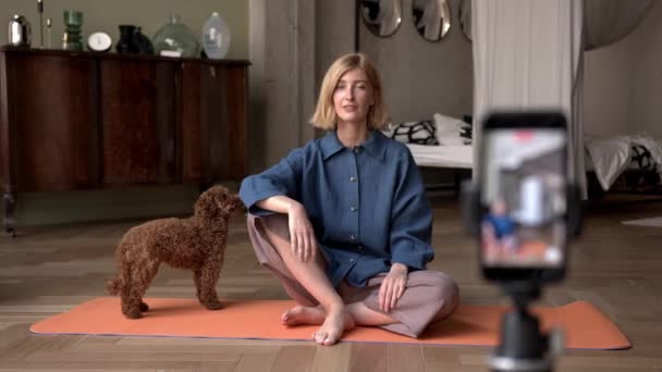 Blond kvinna talar på kameran, sitter på matta med husdjur — Stockvideo