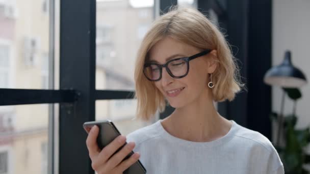 Bizneswoman patrząc na telefon w dłoni ze szczęśliwą twarzą, uśmiechnięta — Wideo stockowe