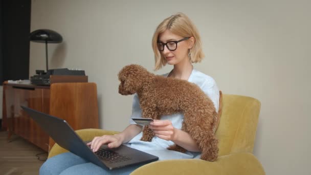 Mulher em óculos com animal de estimação e laptop segurando um cartão de crédito — Vídeo de Stock