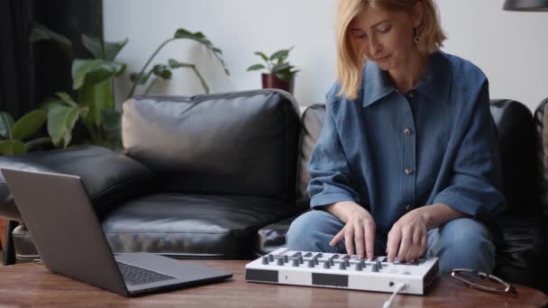 Žena sedí na černé pohovce nahrávání hudby s notebookem, hraje na klávesnici — Stock video