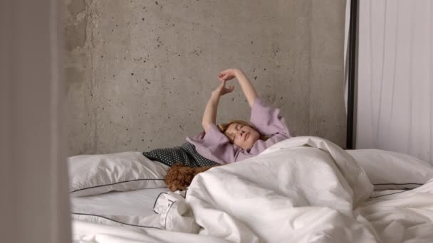Ung kvinna vaknar upp på sängen med hund på vita sängkläder — Stockvideo