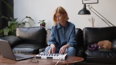 Siyah koltukta oturan bir kadın dizüstü bilgisayarla müzik kaydediyor, melodi çalıyor.