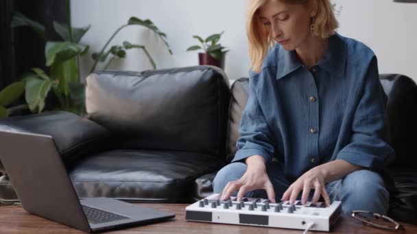 Женщина, сидящая на черном диване, записывает музыку с ноутбука, играет мелодию — стоковое видео