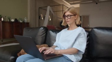 Evdeki kanepede dizüstü bilgisayar ve hayvan kullanan bir kadın.