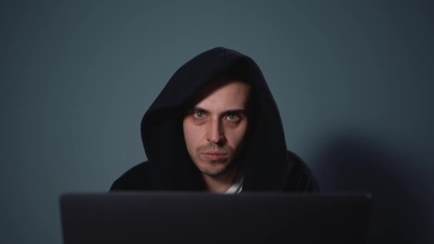 Hackeador nervioso en capucha negra sobre fondo gris trabajando con portátil — Vídeo de stock