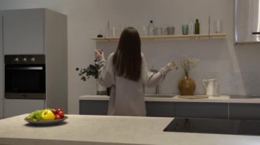 Esmer kadın bir bardak kırmızı şarap içip mutfakta dans ediyor.