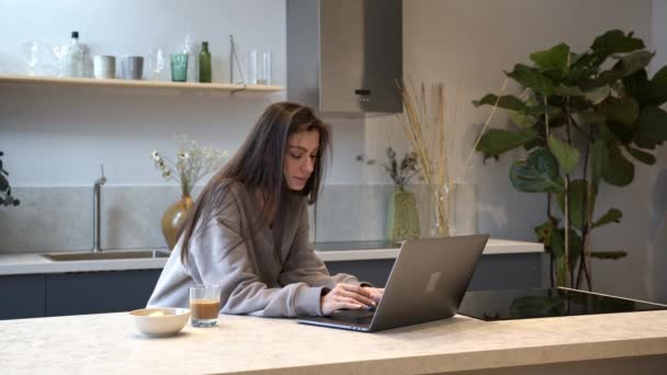 Wanita muda yang sedang sarapan dan mengetik di laptop, minum kopi di dapur — Stok Video