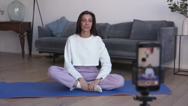 Sport young woman with long hair sitting on a mat, talking in front of the camera — Stock Video