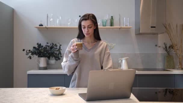 Молодая женщина стоит и пьет утренний кофе глядя на ноутбук — стоковое видео
