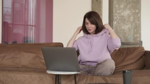 Молода жінка розмовляє на відеодзвінок з ноутбуком у мінімалістичній вітальні — стокове відео