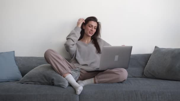 Ev elbiseli genç bir kadın oturma odasındaki dizüstü bilgisayarla video görüşmesi yapıyor. — Stok video