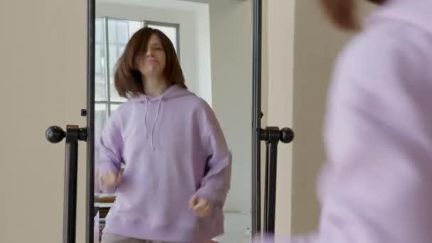 Žena tančící před zrcadlem, usmívající se, v fialové mikině — Stock video