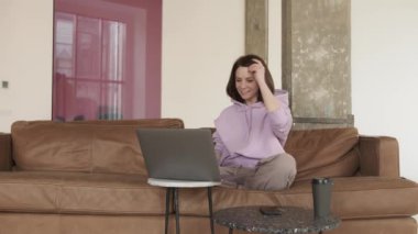 Minimalist oturma odasında dizüstü bilgisayarla konuşan genç bir kadın.