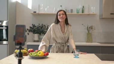 Cep telefonunun önünde konuşan genç bir kadın, masada meyve ve sebzeler.