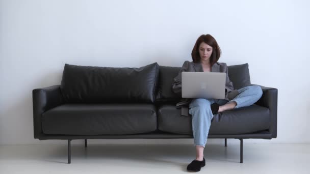 Fiatal üzletasszony dolgozik, ül a fekete kanapén a nappaliban — Stock videók