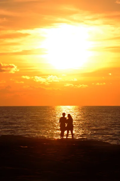 Young couple standing on the shore and looks at the setting sun — Stock Photo, Image
