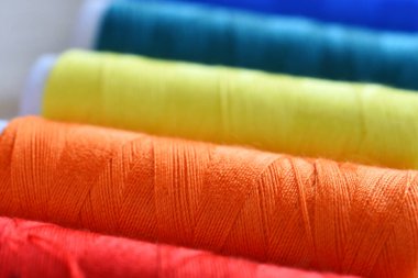 Beyaz ahşap arka planda parlak renkli iplik makaralarının yakın plan görüntüsü. 