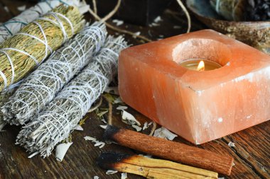 A close up image of a lit selenite candle and sage smudge bundles on a dark wooden table top.  clipart