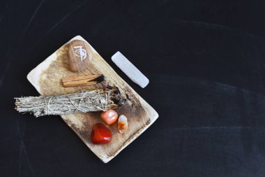 A top view image of a healing smudge kit with white sage and crystals on a black background. 