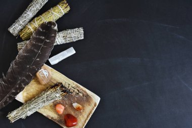 A top view image of a healing smudge kit with white sage and crystals on a black background. 