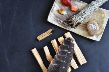 A top view image of a healing smudge kit with white sage and crystals on a black background. 
