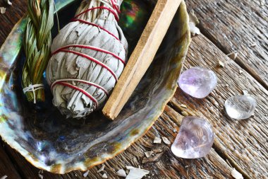 A top view image of three different smudge sticks in an abalone shell with healing crystals. 