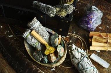 A close up image of white sage smudge sticks with rough crystals and selenite on a dark wooden table. 