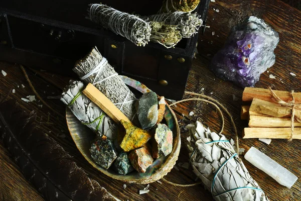 A close up image of white sage smudge sticks with rough crystals and selenite on a dark wooden table. 