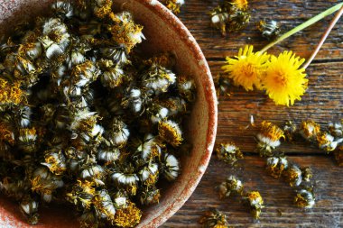 Koyu kırsal bir masada kurutulmuş karahindiba çiçekleriyle dolu el yapımı bir çanak çömlek resmi.. 