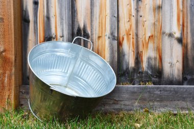 Tahta bir çite dayanmış galvanize olmuş eski bir küvet görüntüsü.. 