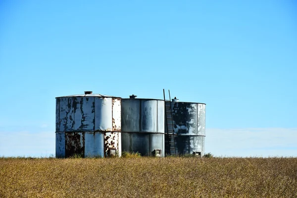 An image of metal grain silos in a agricultural field during harvest season.