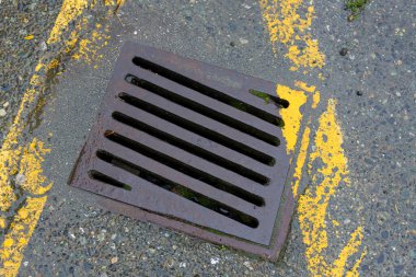 Eski sarı renkli park şeritleri olan kare bir yağmur suyu giderinin en üst görüntüsü..