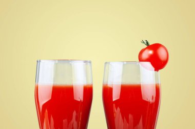 İki bardak domates suyu ve sarı arka planda küçük bir domates..