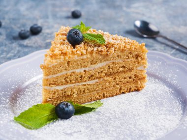 Gri arka planda yaban mersinli bir dilim ekşi kremalı ballı pasta.