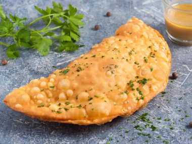 Et ve hardal soslu lezzetli bir cheburek, gri arka planda yeşilliklerle süslenmiş.