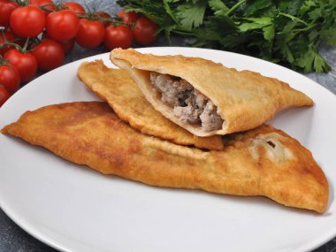 Sebze ve otlarla süslenmiş beyaz bir tabakta sığır eti ve domuz etiyle nefis bir cheburek.