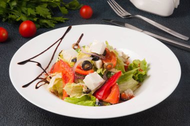 Siyah arka planda beyaz tabakta lezzetli Yunan salatası.