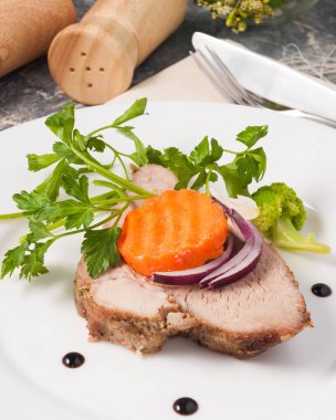 Beyaz bir tabakta havuç ve otlarla süslenmiş lezzetli bir parça haşlanmış biftek.