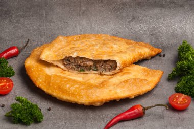 Gri arka planda domuz eti ve sığır etli lezzetli bir cheburek.