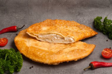 Bitki ve sebzelerle süslenmiş gri arka planda tavuklu lezzetli bir cheburek.