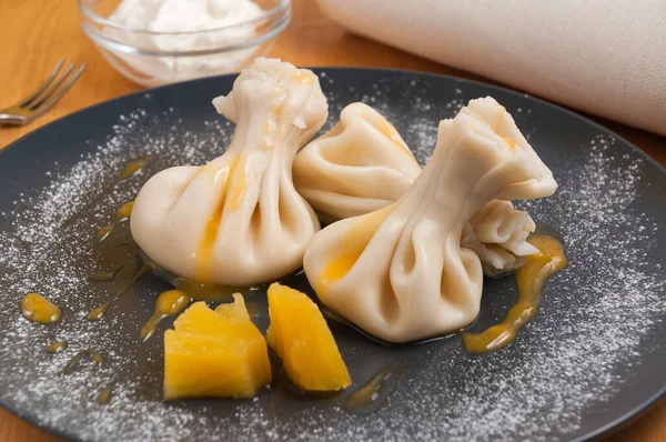 Ananaslı tatlı khinkali ve siyah tabakta süzme peynir.
