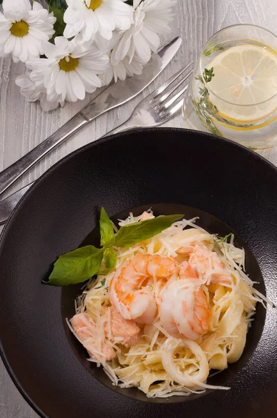 tasty pasta with seafood: salmon, squid, king prawns on a black plate. Top view