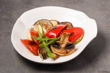 Beyaz bir tabakta lezzetli patlıcan, kabak, biber ve ızgara mantar.