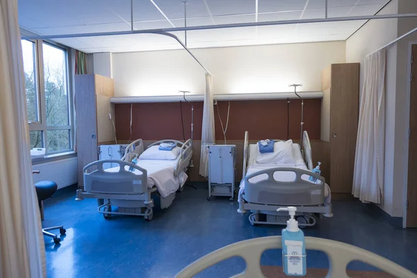 Interior  of an empty hospital room with two made beds seen from another bed across the room